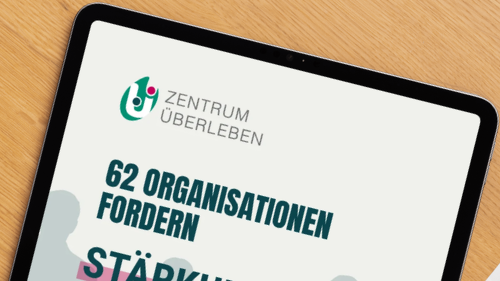 Ein Tablet auf einem Holzschreibtisch zeigt das Titelblatt einer Publikation des Zentrum Überleben mit der Überschrift „62 Organisationen fordern Stärkung zivilgesellschaftlicher Organisationen in der Arbeit mit geflüchteten Menschen“. Im Hintergrund des Titelblatts sind stilisierte Silhouetten von mehreren Menschen abgebildet, die Hand in Hand nebeneinander stehen.