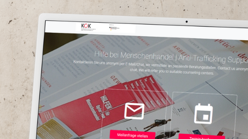 Alt-Text:  Desktop-Monitor auf einem Schreibtisch. Auf dem Bildschirm die Startseite der Online Anlaufstelle Menschenhandel des KOK. &Uuml;berschrift Hilfe bei Menschenhandel. Zwei gro&szlig;e Schaltfl&auml;chen mit Symbolen f&uuml;r E Mail Anfrage stellen und Termin buchen. Im Hintergrund liegen Informationsmaterialien und Flyer.