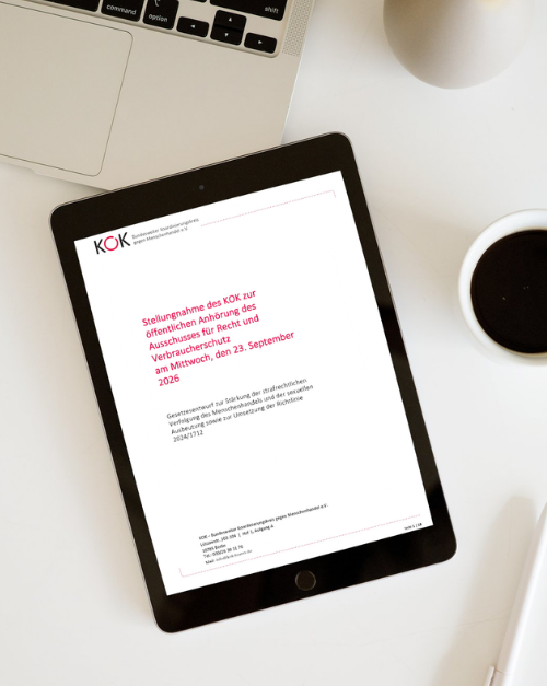 Ein Tablet auf einem wei&szlig;en Schreibtisch zeigt die Titelseite einer Stellungnahme des KOK. Der Titel lautet: &bdquo;Stellungnahme des KOK zur &ouml;ffentlichen Anh&ouml;rung des Ausschusses f&uuml;r Recht und Verbraucherschutz am Mittwoch, den 23. September 2026&ldquo;. Auf dem Tisch sind au&szlig;erdem Teile eines Laptops und eine Tasse Kaffee zu sehen.
